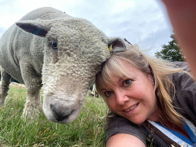 Photograph of lady and sheep  with their heads resting together.